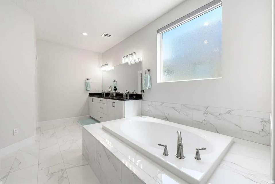 Full bathroom with double vanity, a bath, and light marble finish flooring
