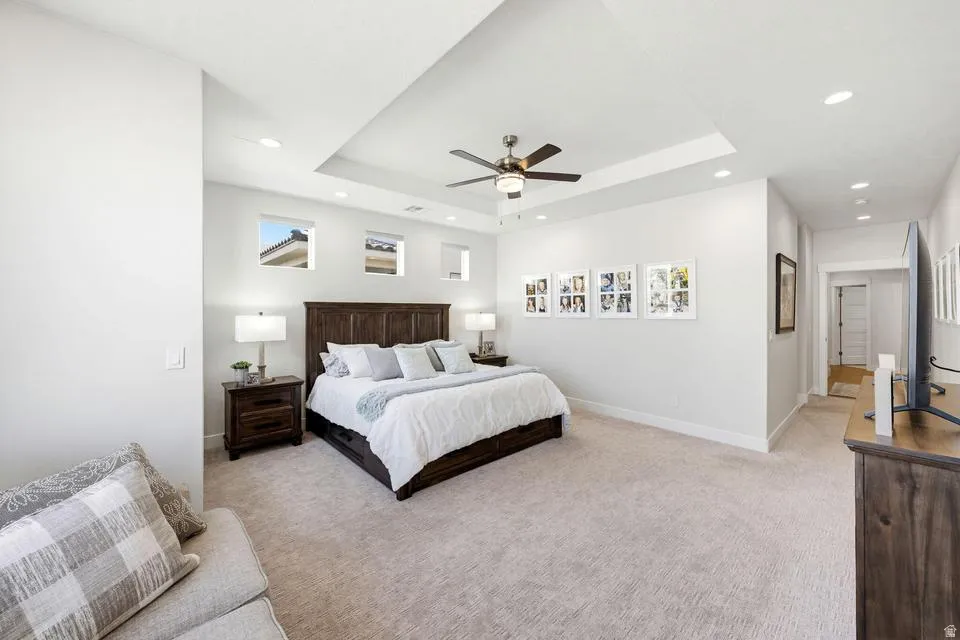 Bedroom with light carpet, a ceiling fan, a tray ceiling, and recessed lighting
