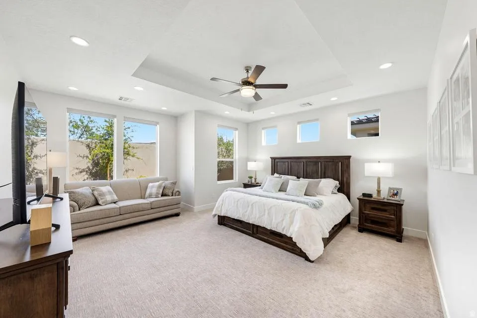 Bedroom with a tray ceiling, light carpet, a ceiling fan, and recessed lighting