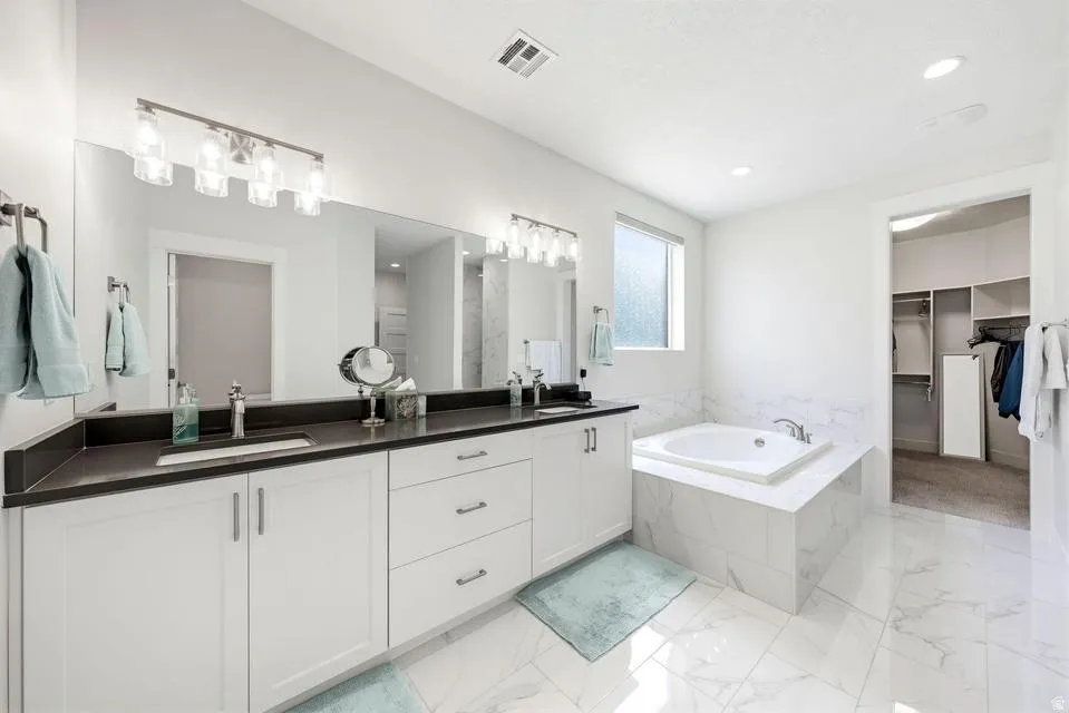 Full bathroom with a walk in closet, double vanity, light marble finish flooring, and a bath