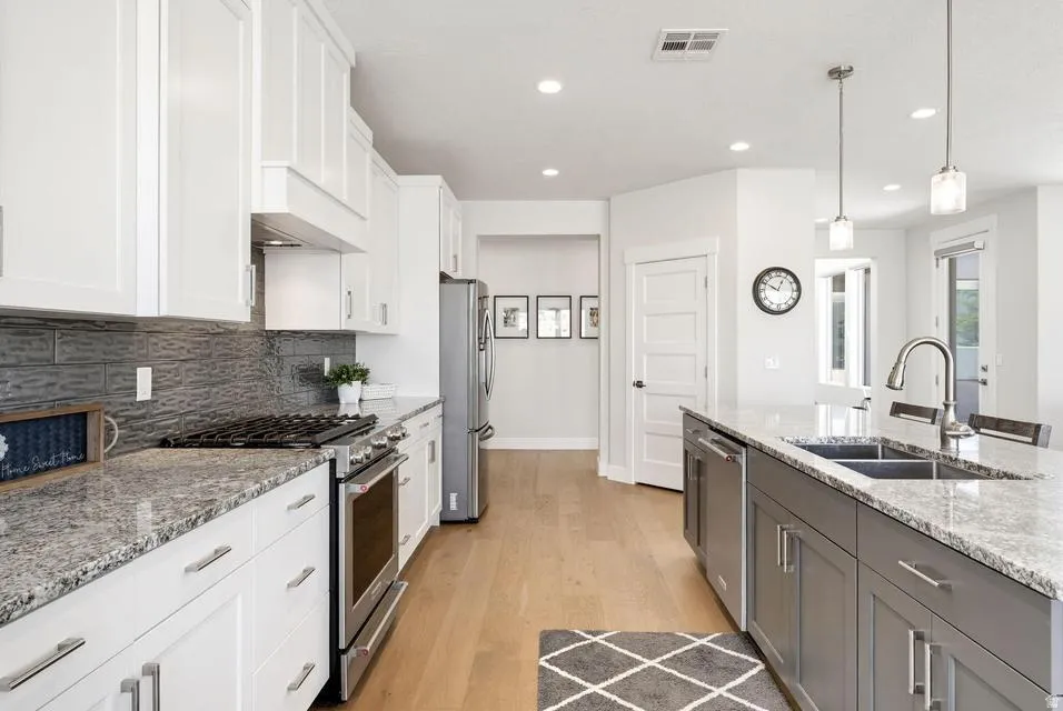 Kitchen featuring stainless steel appliances, light stone countertops, two tone cabinets, light wood-type flooring, and hanging light fixtures