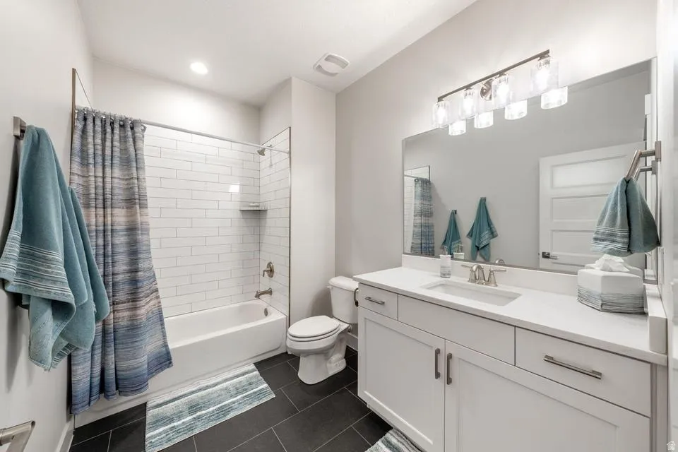 Full bathroom with vanity, shower / tub combo with curtain, and dark tile patterned flooring