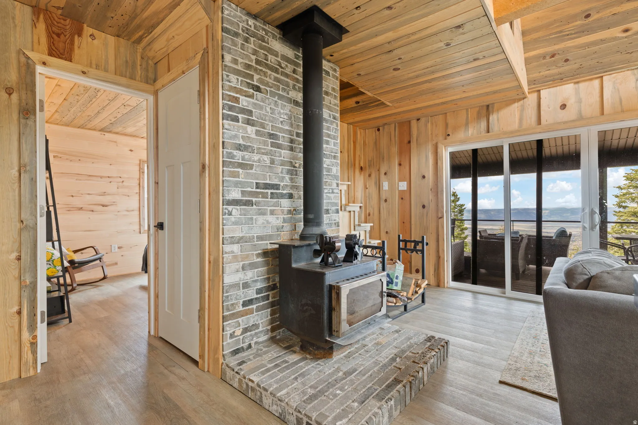 Cabin 1 - West; Living area with wooden ceiling, wooden walls, a wood stove, and light wood-style flooring