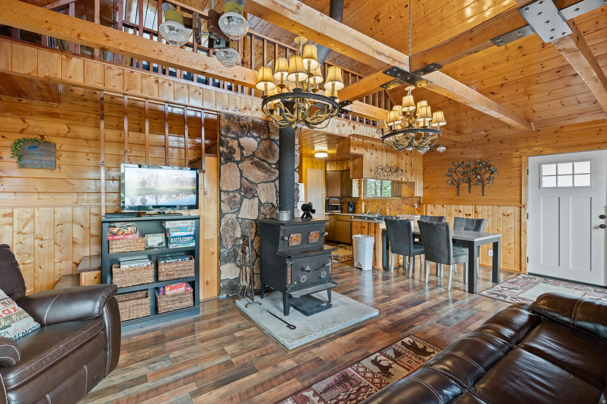 Cabin 2 - East; Living area featuring wooden walls, suspended lighting, hardwood / wood-style flooring, a high wooden beamed ceiling, and a wood stove