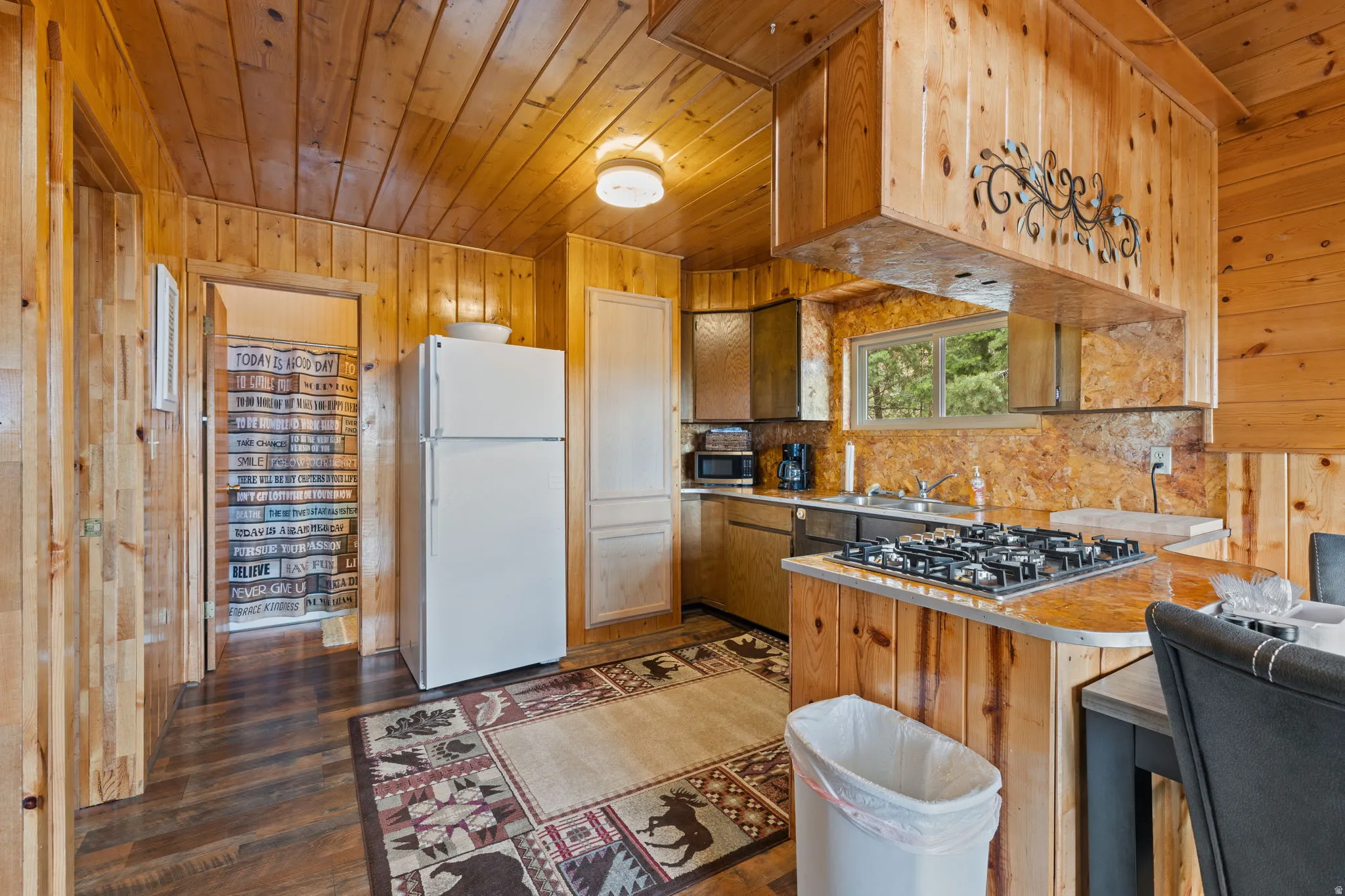 Cabin 2 - East; Kitchen with a peninsula, wooden walls, a breakfast bar area, and dark wood-style flooring