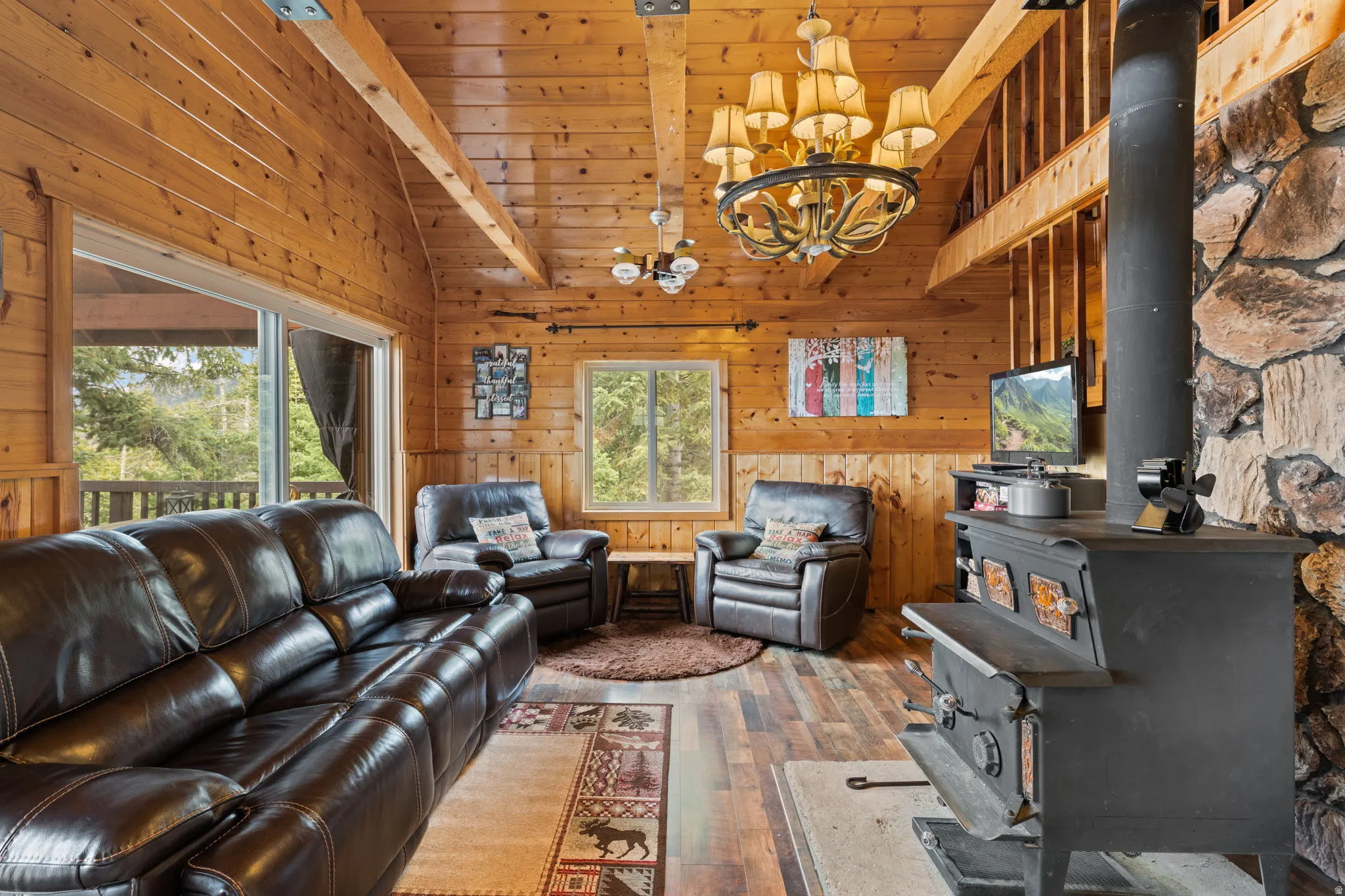 Cabin 2 - East; Living room featuring wood walls, a chandelier, a wood stove, hardwood / wood-style floors, and a high wood beamed ceiling