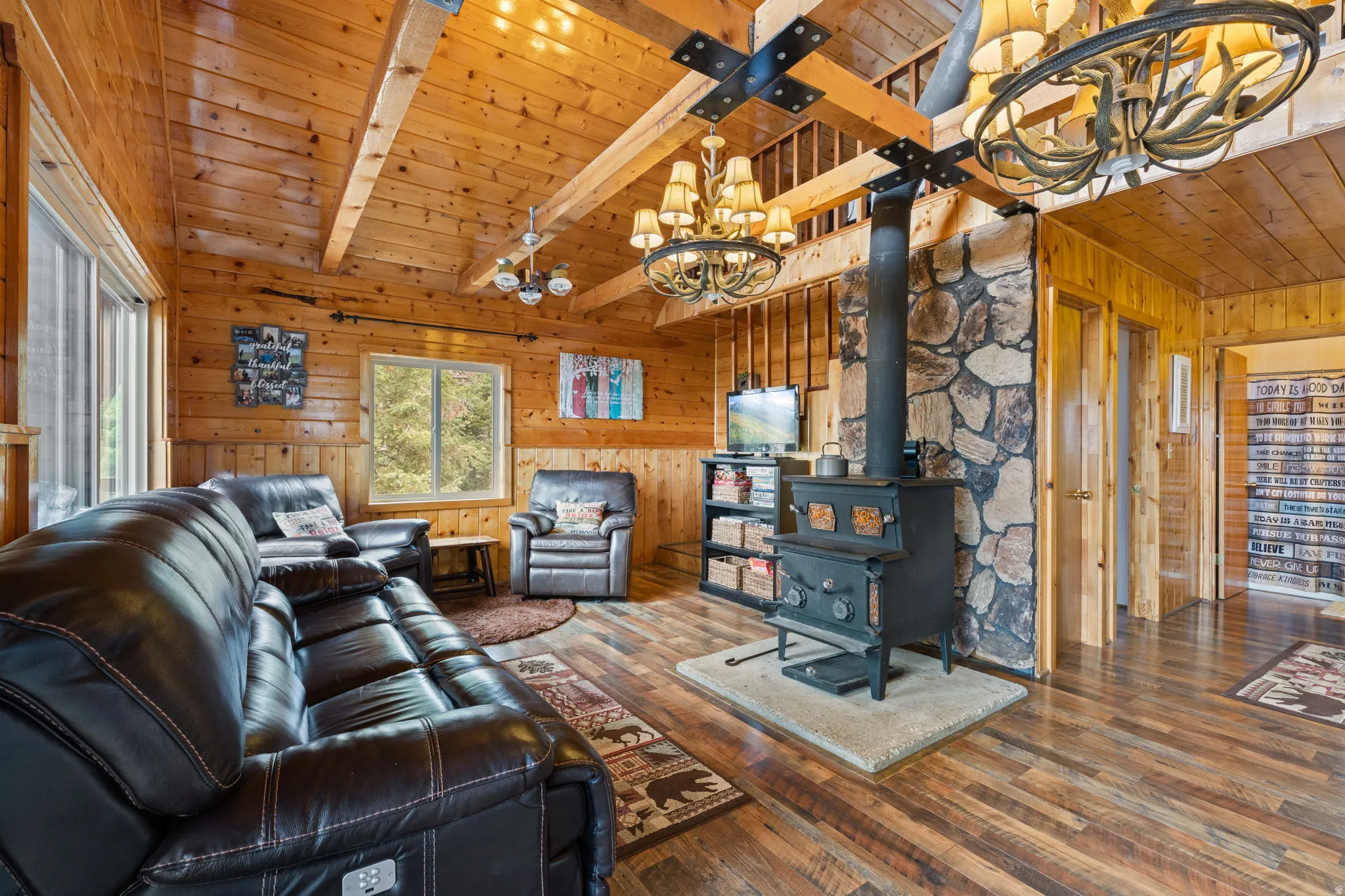 Cabin 2 - East; Living room with a chandelier, a wooden ceiling with exposed beams, wood-type flooring, wood walls, and a wood stove