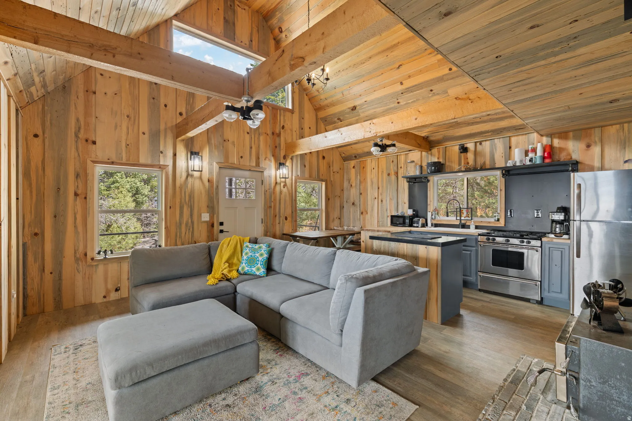 Cabin 1 - West; Living room featuring plenty of natural light, wooden walls, a ceiling fan, a high wooden beamed ceiling, dark wood-style flooring and wood burning stove