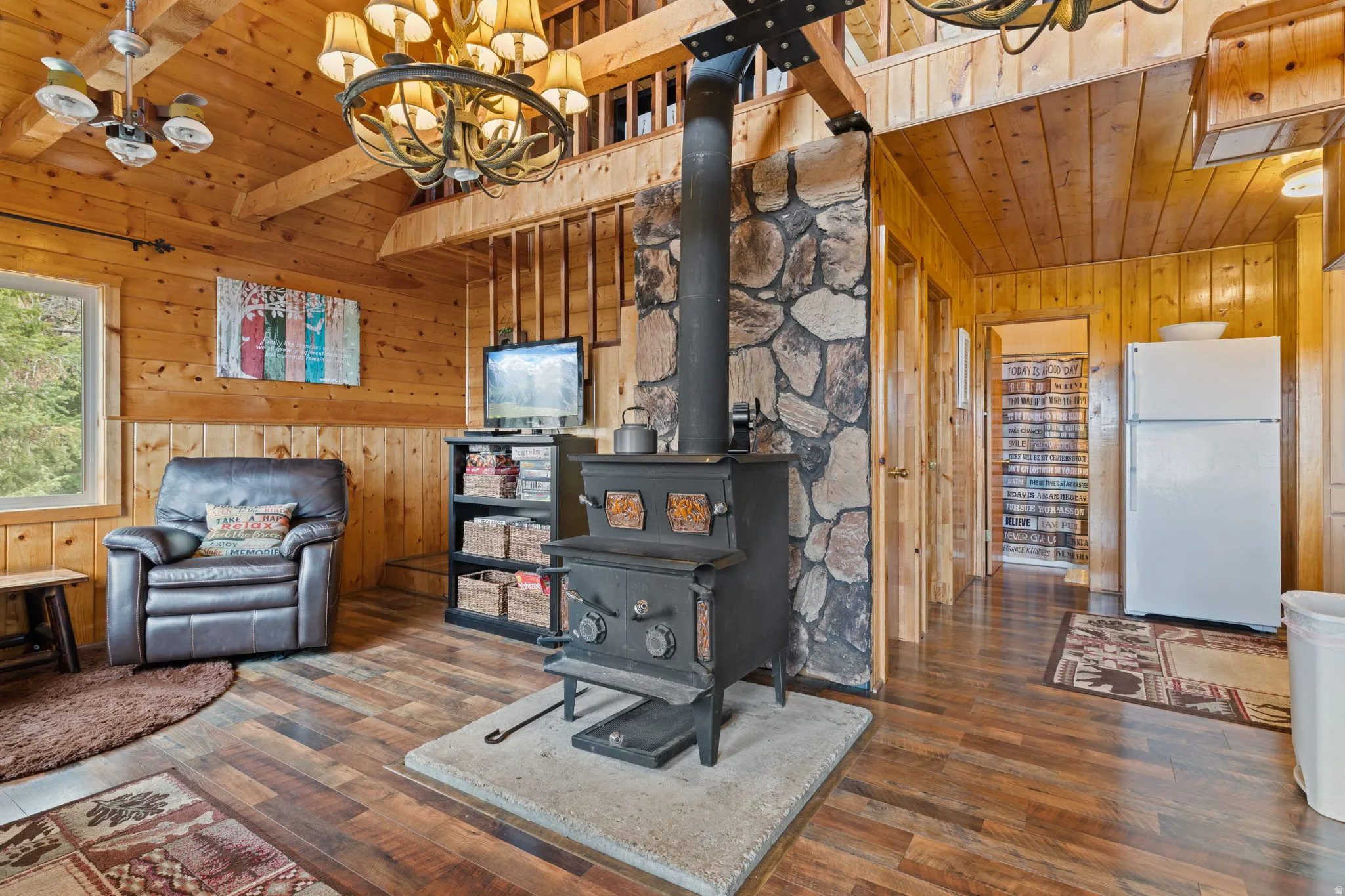 Cabin 2 - East; Sitting room with wooden ceiling, suspended lighting, dark wood-type flooring, wood walls, and a wood stove