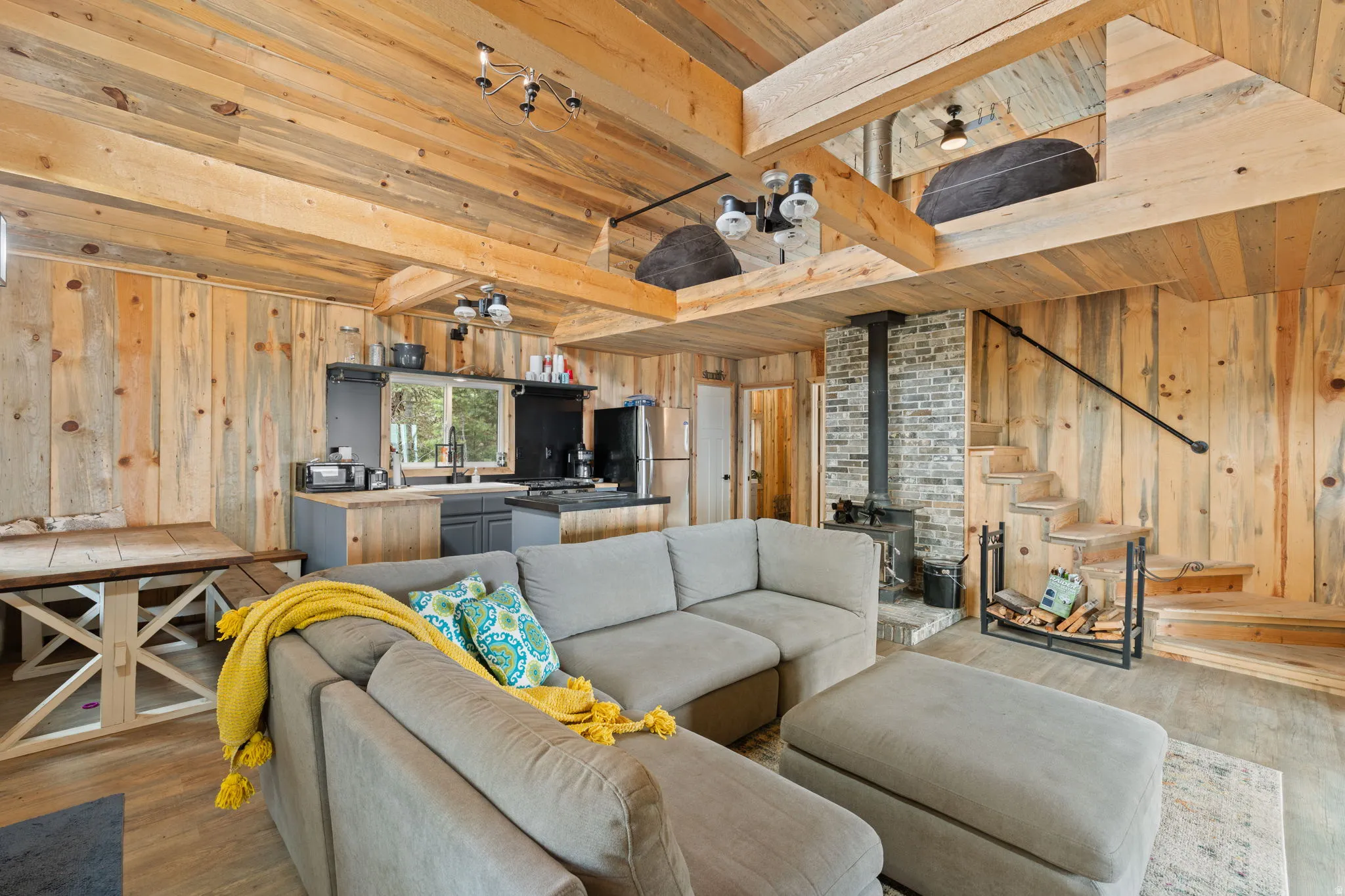 Cabin 1 - West; Living area featuring wooden walls, a wood stove, wood finished floors, and a wooden ceiling with exposed beams