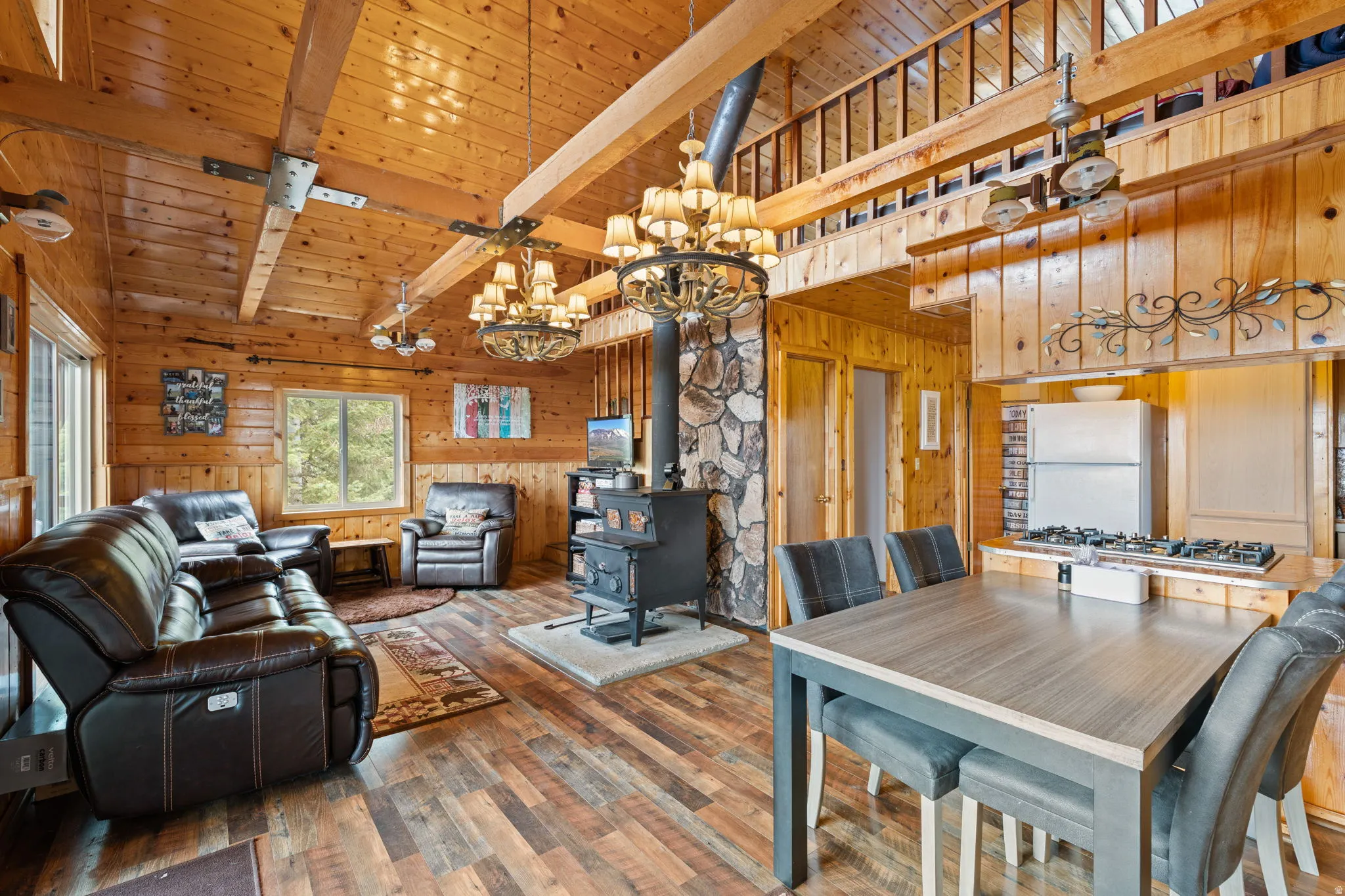 Cabin 2 - East; Living area with hanging lights, a wood stove, wood-type flooring, wooden walls, and a high wood beamed ceiling
