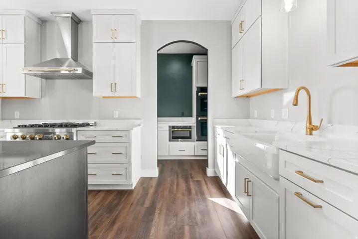 Kitchen featuring dark wood-type flooring, light stone countertops, two tone cabinetry, arched walkways, and stainless steel gas range