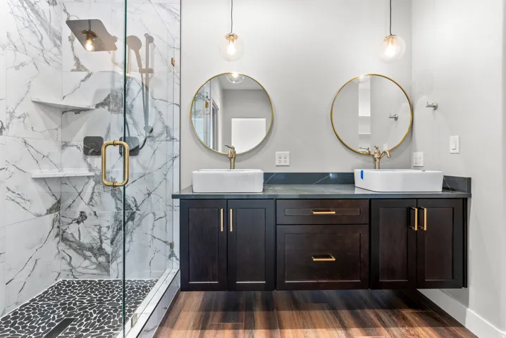 Full bath featuring double vanity, a marble finish shower, and dark wood-type flooring