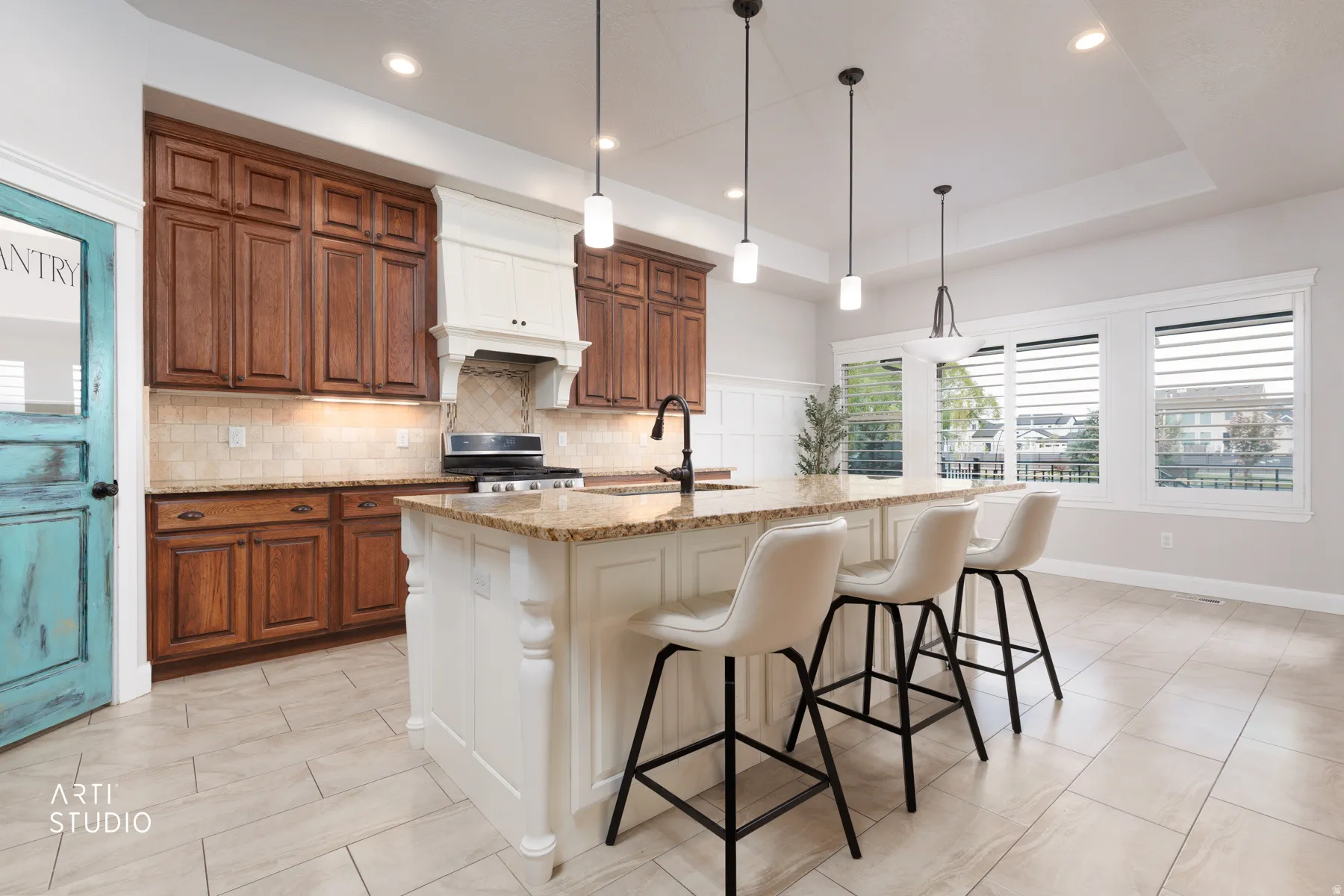 Two tone kitchen with two tone cabinetry, light stone countertops, a kitchen bar, decorative light fixtures, and an island with sink