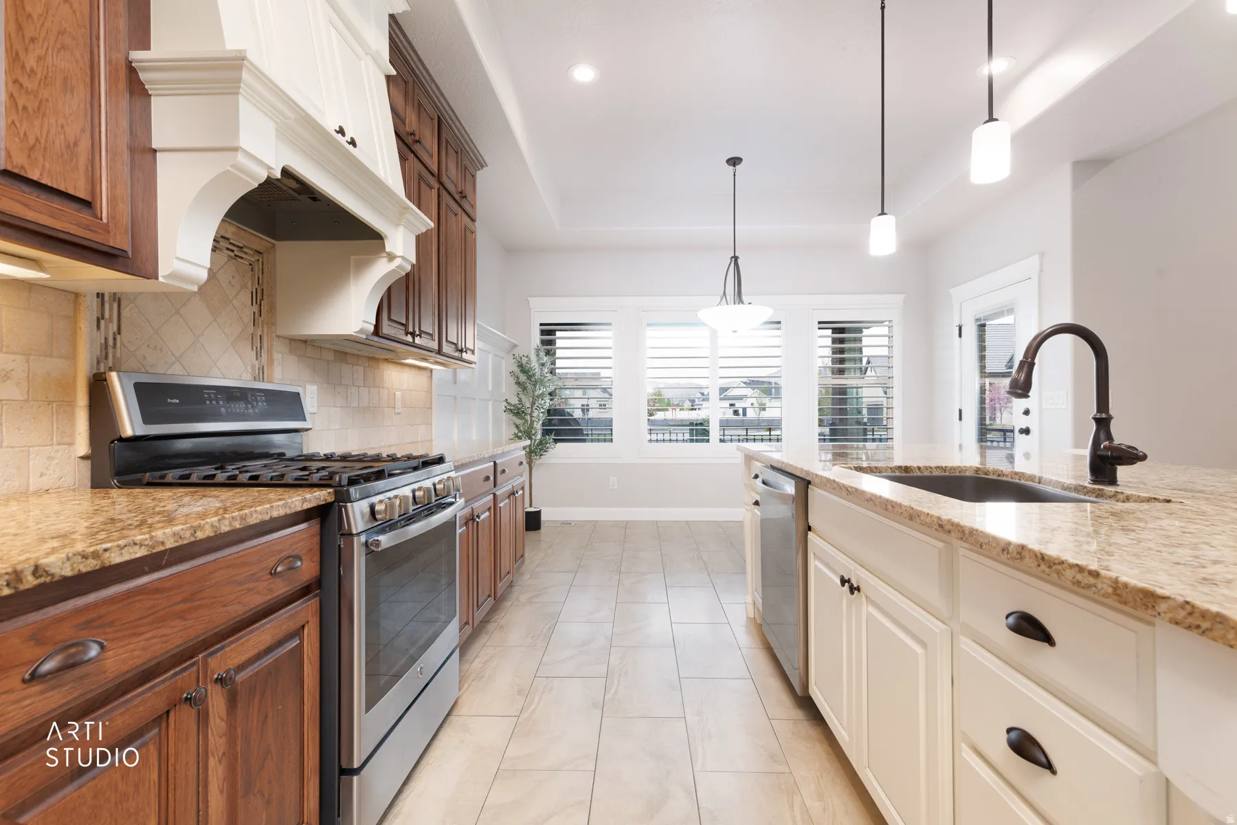 Dual tone kitchen with stainless steel appliances, light stone countertops, a tray ceiling, two tone cabinets, and backsplash