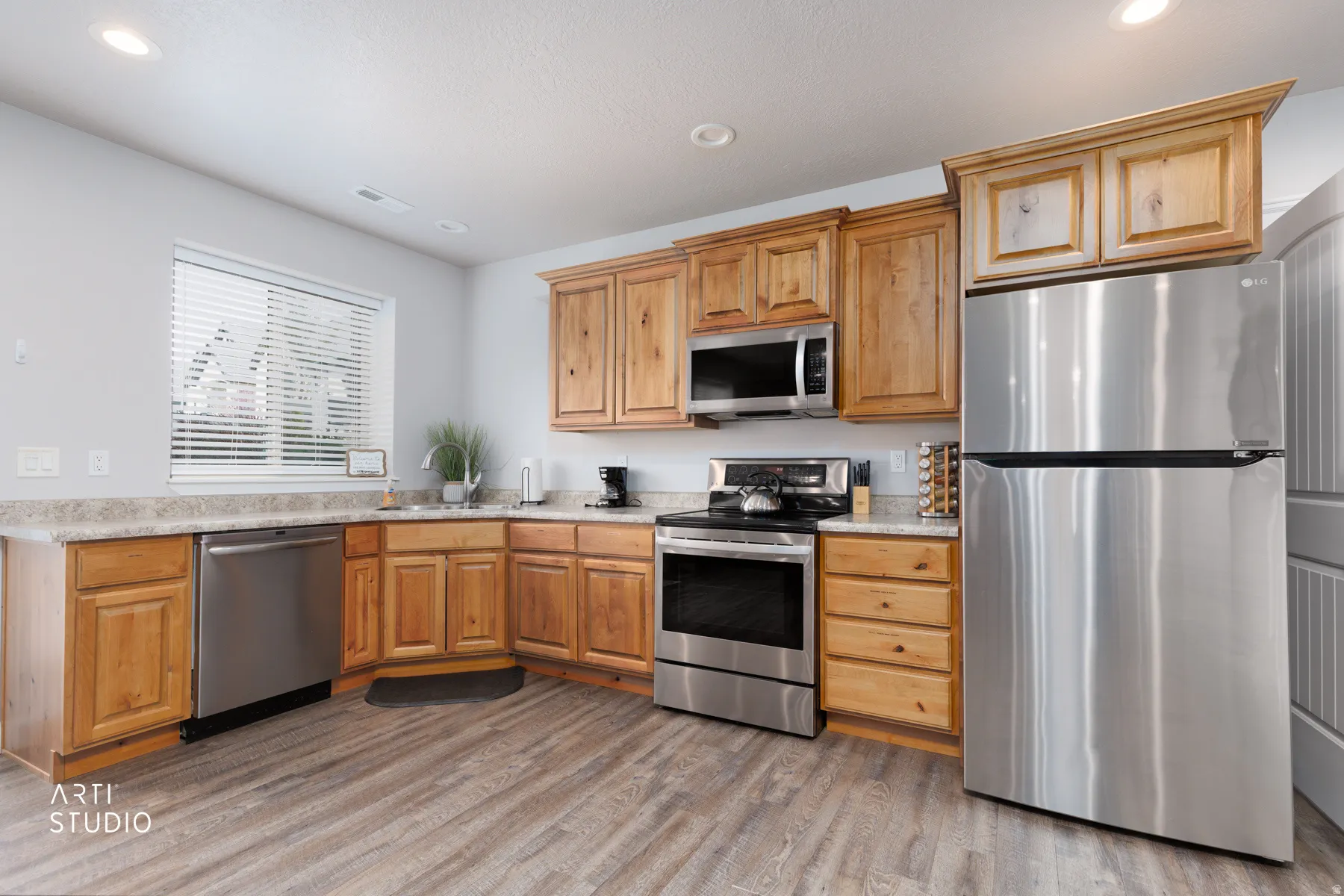 Kitchen with stainless steel appliances, recessed lighting, light wood-type flooring, and light stone countertops