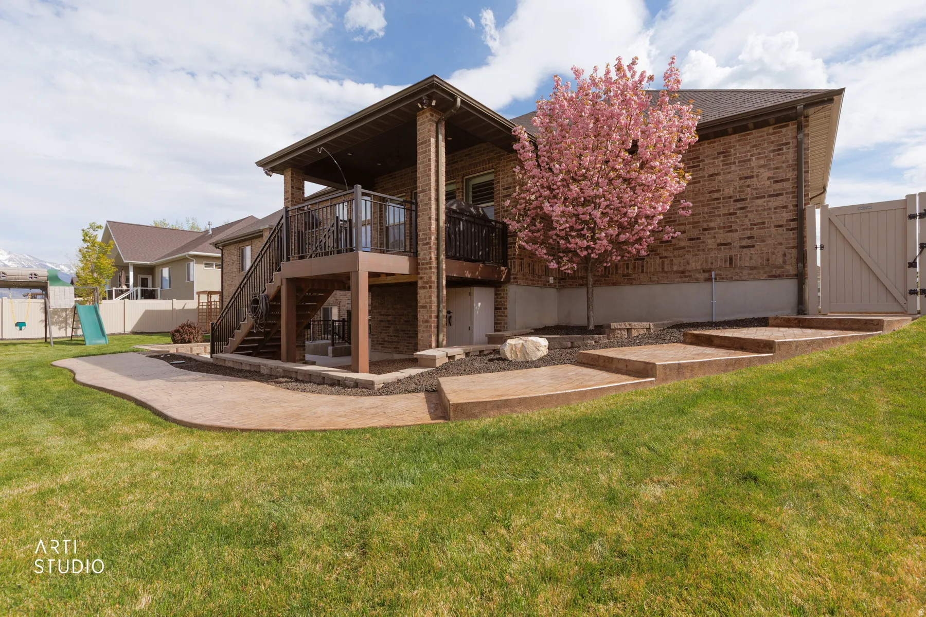 Rear view of house featuring a patio area, a gate, brick siding, and a wooden deck