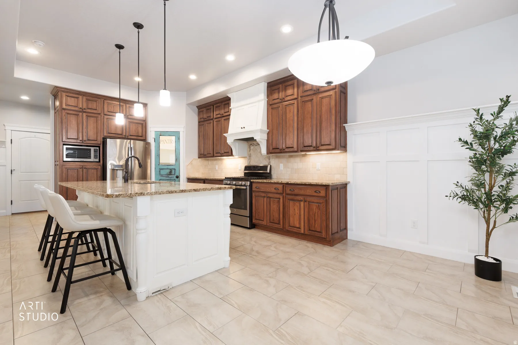 Kitchen featuring two tone cabinetry, light stone countertops, a kitchen bar, stainless steel appliances, and an island with sink