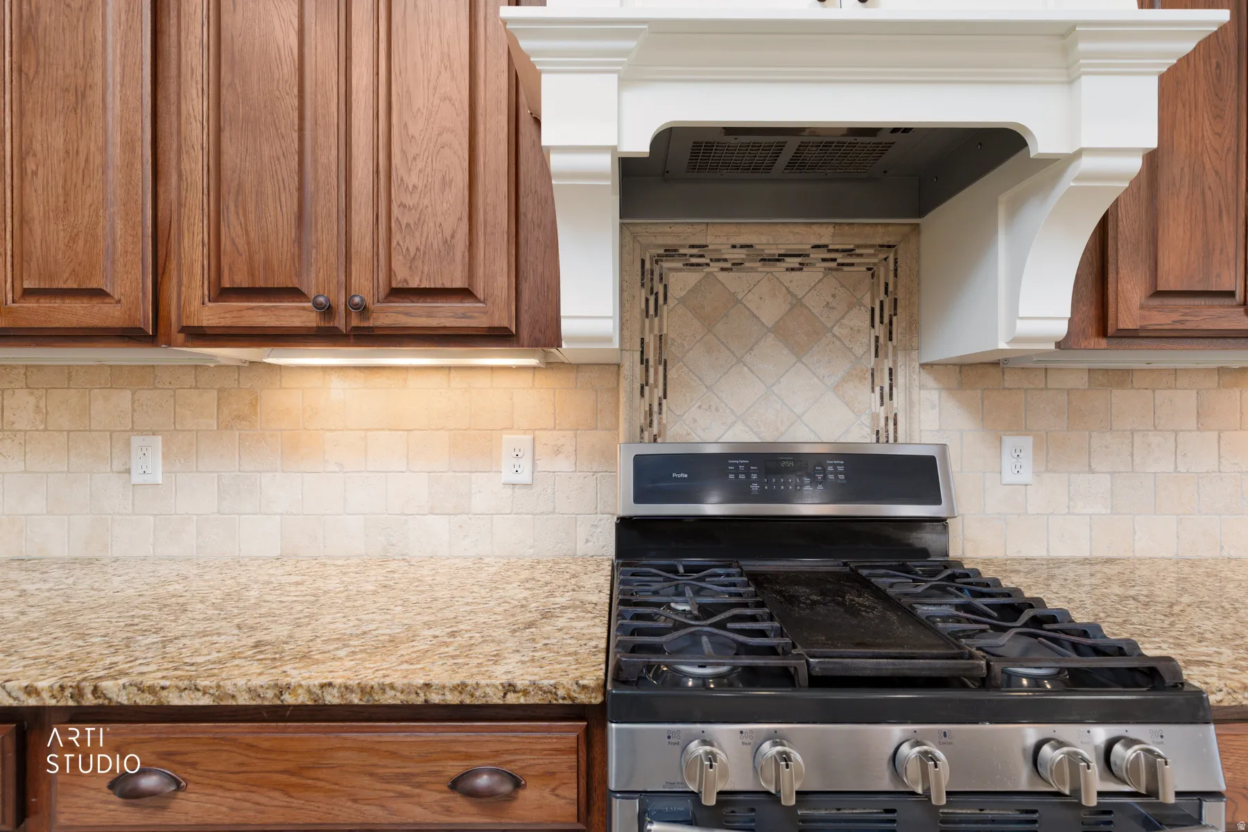 Kitchen with gas stove, light stone counters, backsplash, and wood finish cabinetry