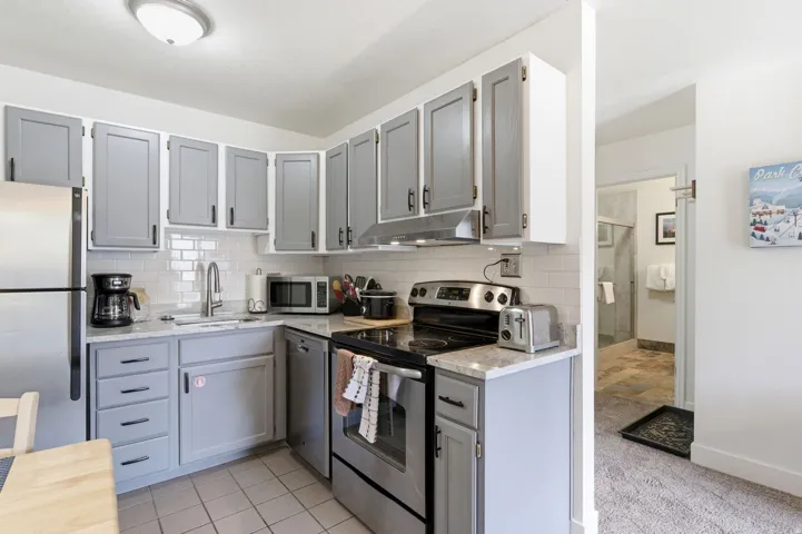 Kitchen with gray cabinets, stainless steel appliances, light stone countertops, and decorative backsplash