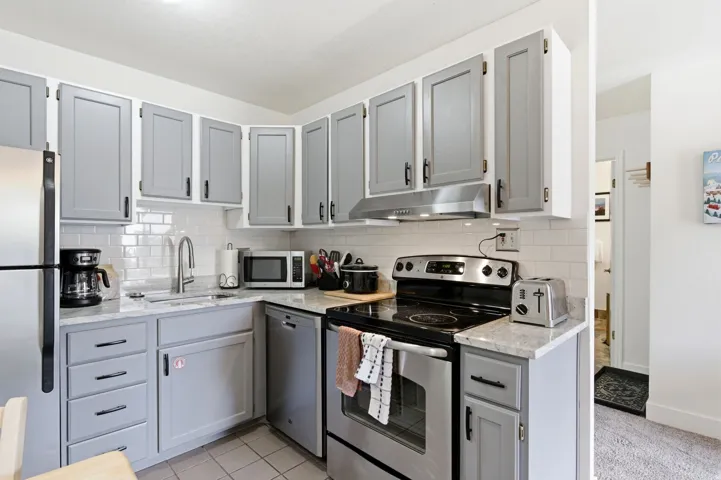 Kitchen with gray cabinetry, stainless steel appliances, light stone countertops, tasteful backsplash, and light tile patterned floors