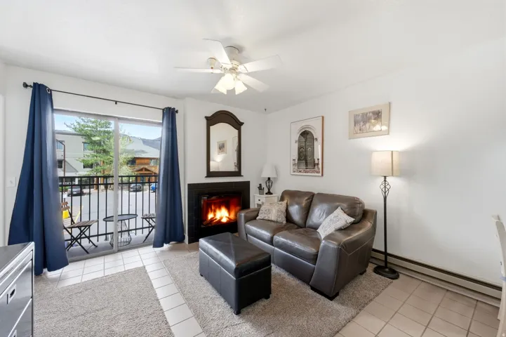 Living room with light tile patterned floors, baseboard heating, a ceiling fan, and a lit fireplace