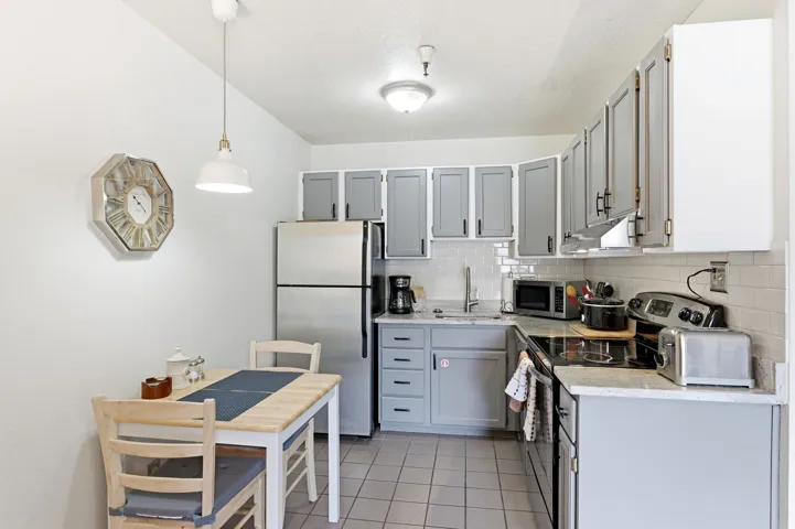 Kitchen with stainless steel appliances, gray cabinets, light tile patterned floors, and backsplash