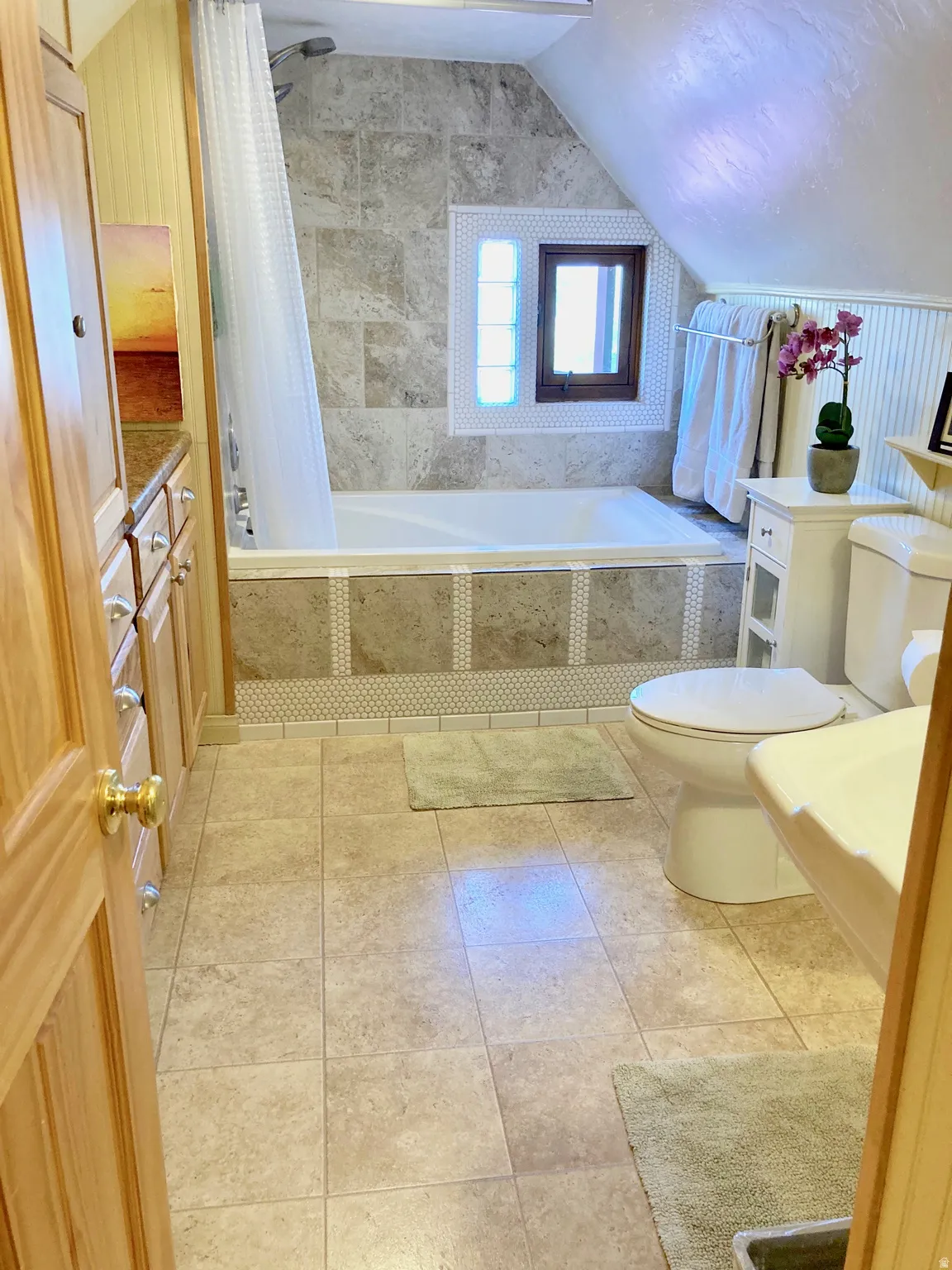 Full bathroom featuring tiled shower / bath, lofted ceiling, vanity, and light tile patterned floors
