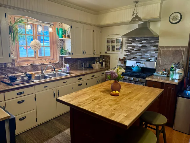 Dual tone kitchen with butcher block countertops, gas range, a kitchen island, backsplash, and two tone cabinets