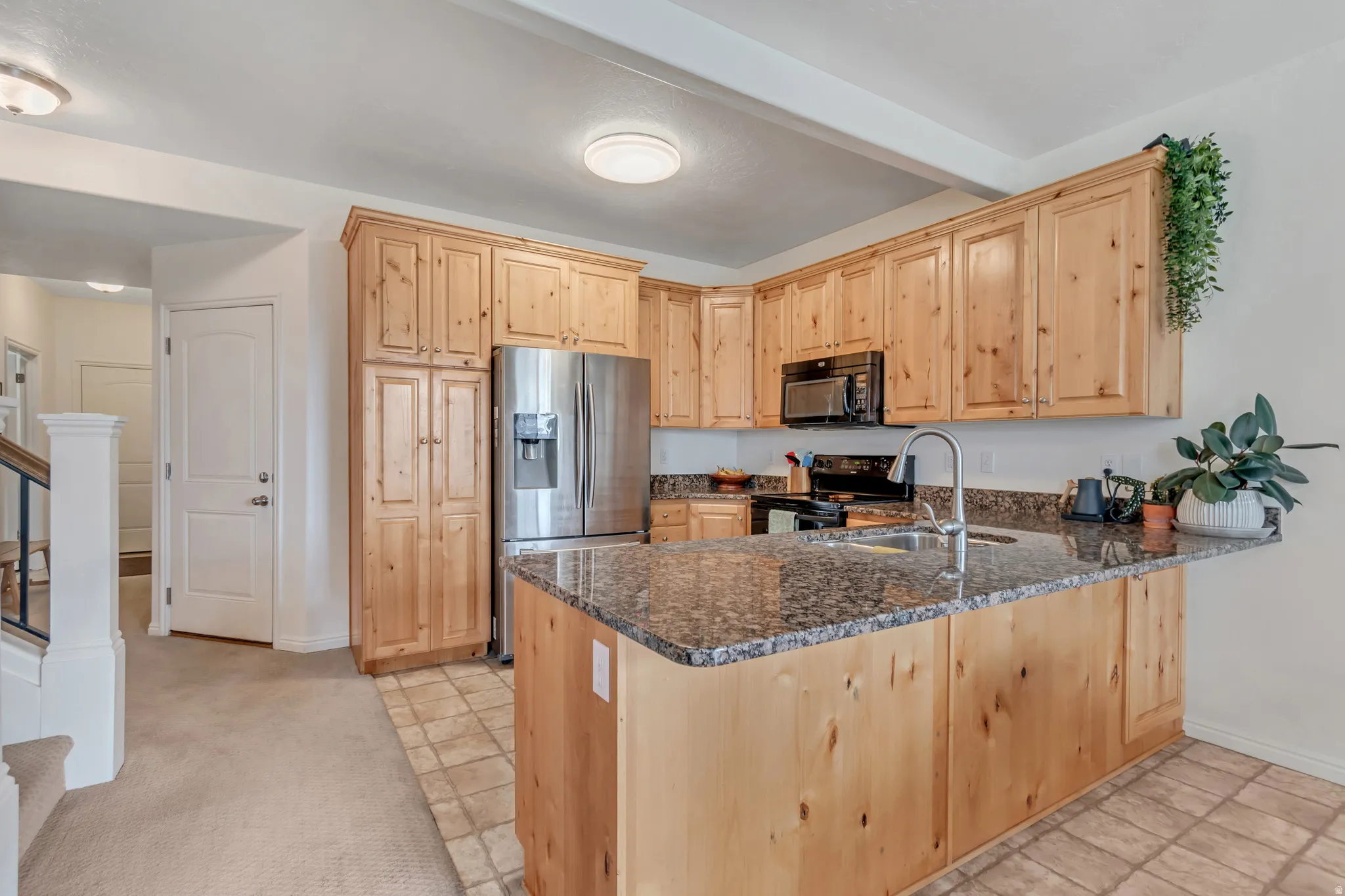 Kitchen with light wood finish cabinets, dark granite countertops, and included appliances.
