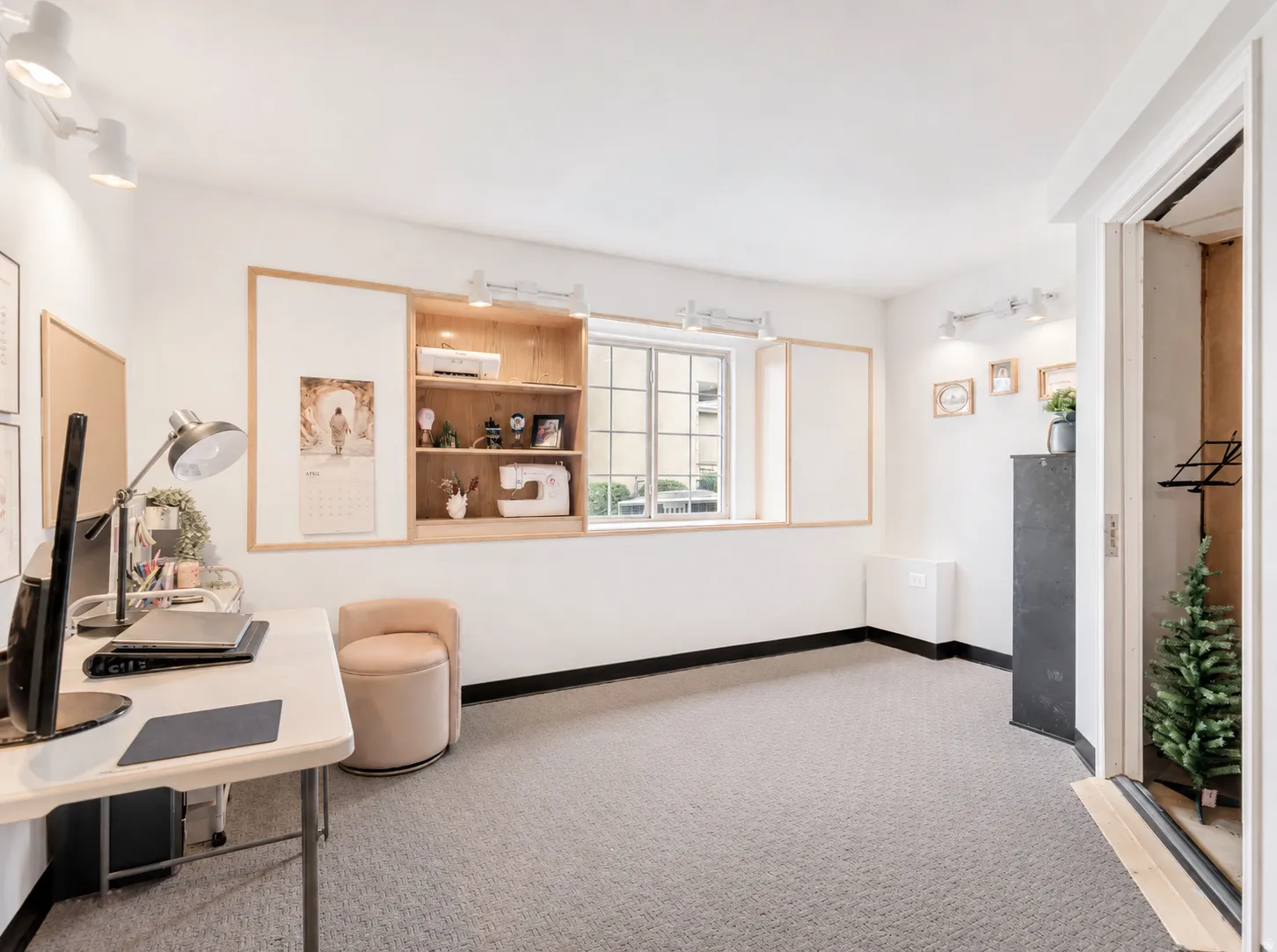Spacious room with light-colored carpeting, built-in wooden shelving, track lighting, and a window providing natural illumination