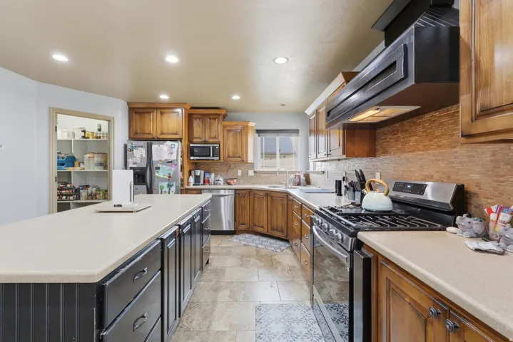 Dual tone kitchen with stainless steel appliances, ventilation hood, light countertops, a center island, and decorative backsplash