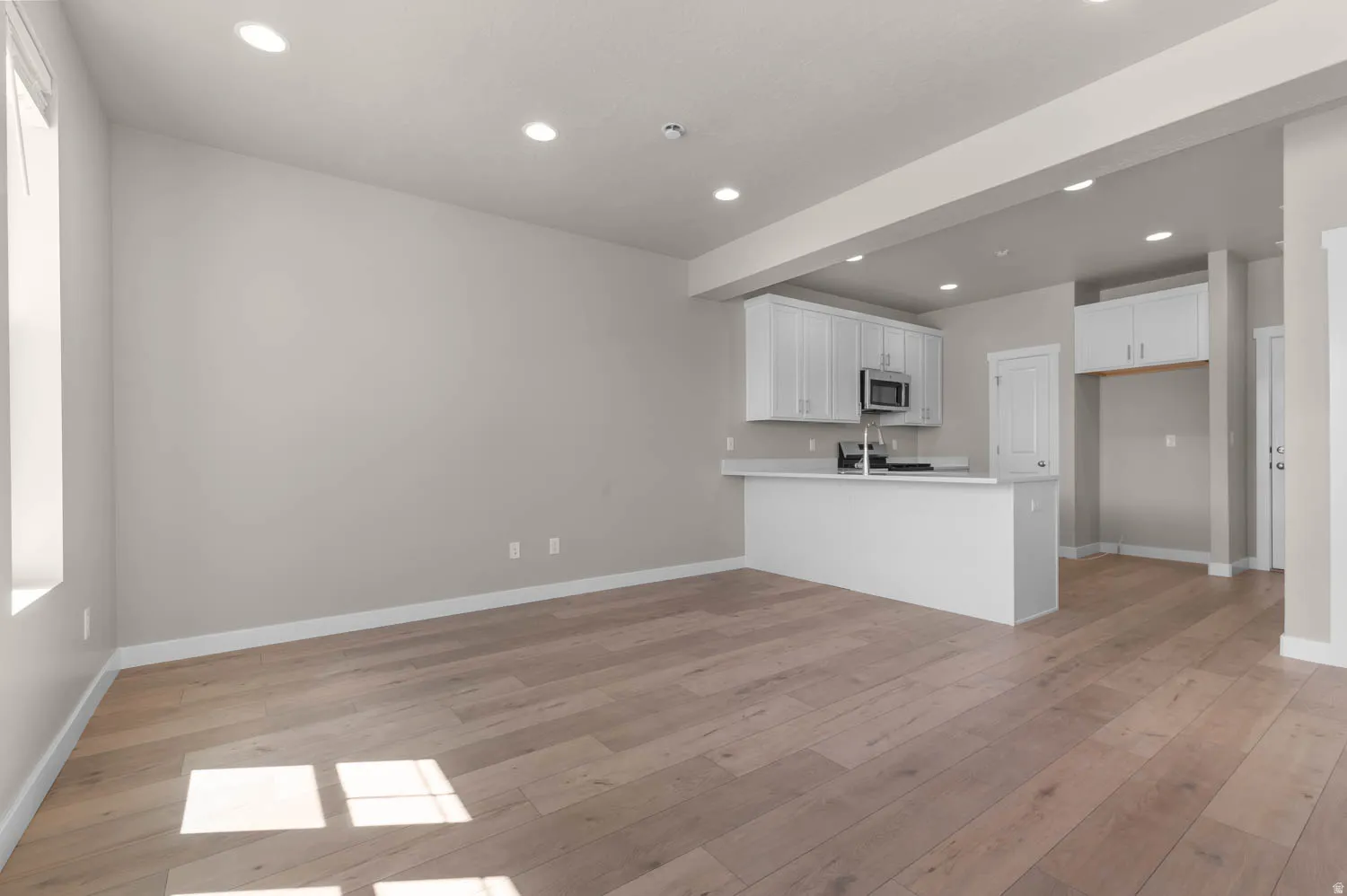 Kitchen featuring a peninsula, white cabinets, light countertops, light wood finished floors, and recessed lighting