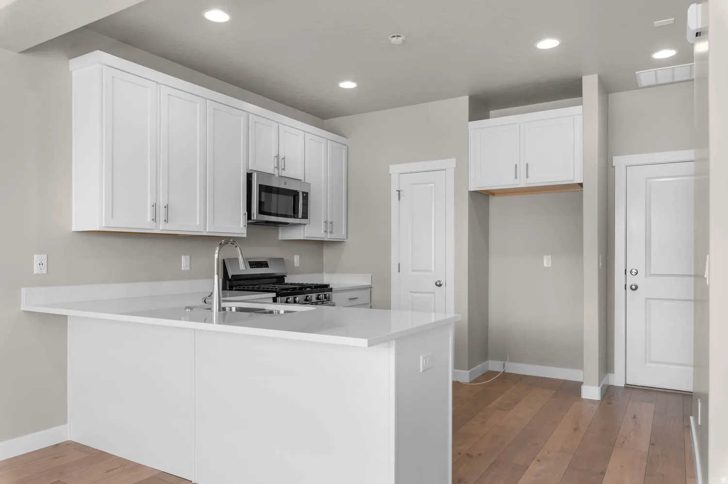 Kitchen featuring white cabinets, light wood-style flooring, stainless steel appliances, a peninsula, and recessed lighting