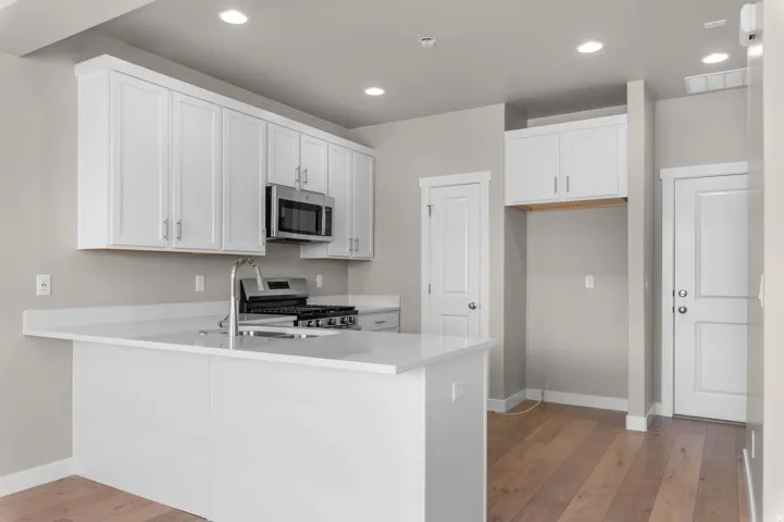 Kitchen featuring white cabinets, light wood-style flooring, stainless steel appliances, a peninsula, and recessed lighting
