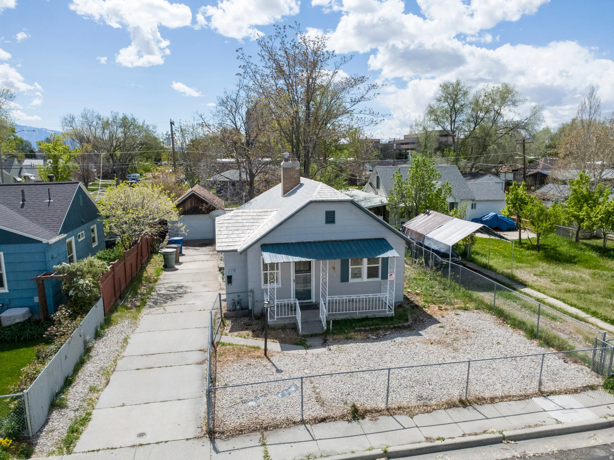 Bungalow-style home with a fenced front yard, covered porch, a residential view, a chimney, and a metal roof