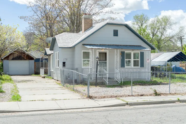 Bungalow-style home featuring a porch, an outdoor structure, a fenced front yard, a chimney, and concrete driveway