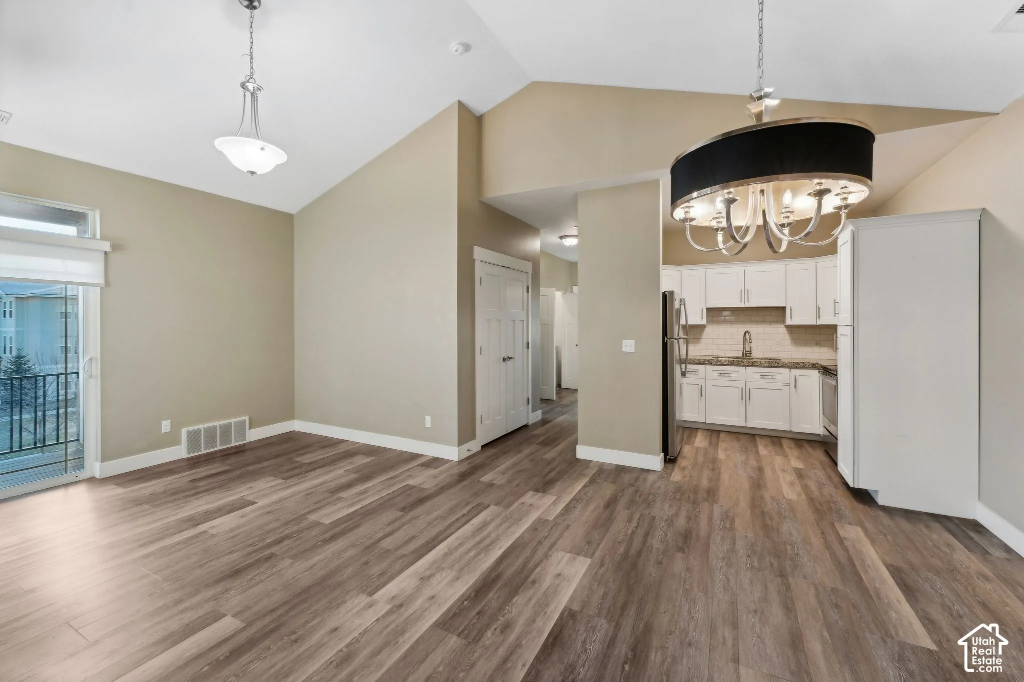 Kitchen with suspended lighting, white cabinetry, vaulted ceiling, dark wood-style floors, and backsplash