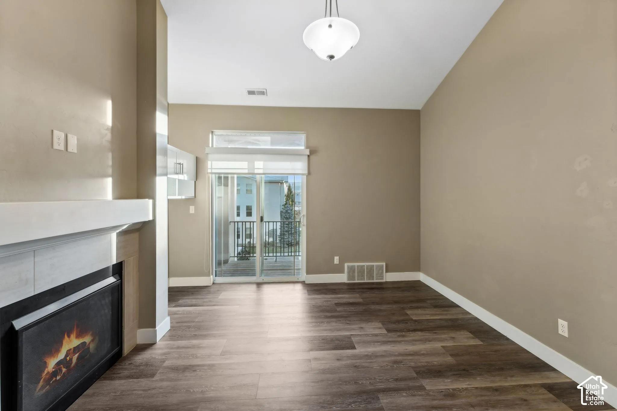 Unfurnished living room with dark wood-type flooring, a lit fireplace, and lofted ceiling