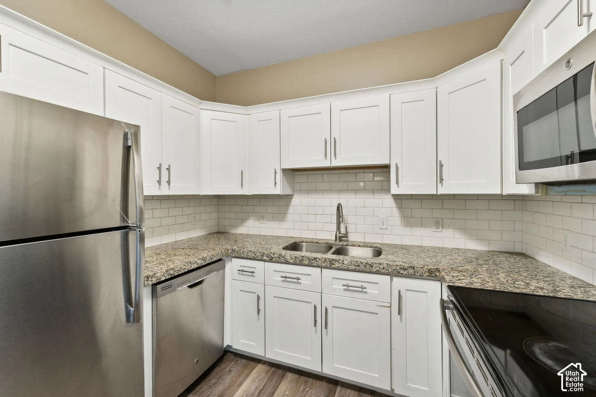 Kitchen featuring stainless steel appliances, white cabinets, light stone countertops, and dark wood-type flooring