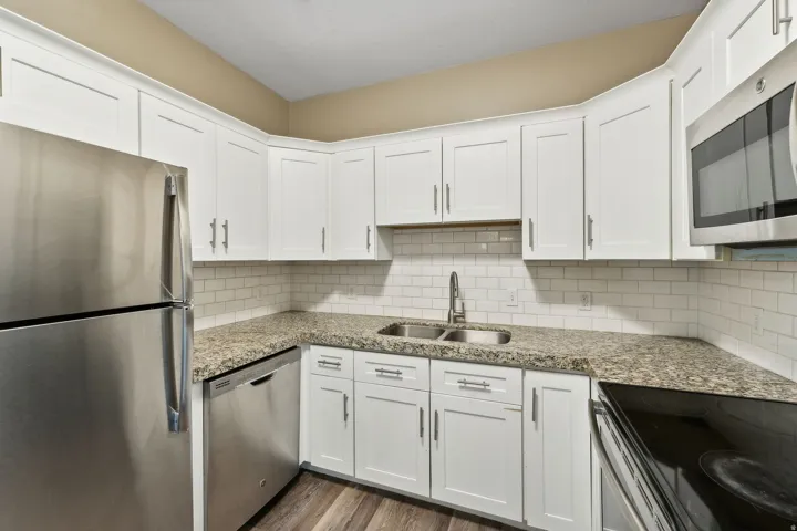 Kitchen featuring stainless steel appliances, white cabinets, light stone countertops, and dark wood-type flooring