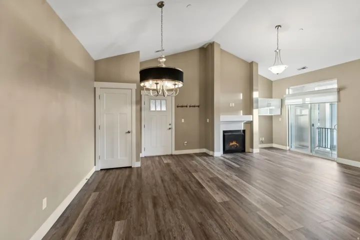 Unfurnished living room with dark wood-style floors, a high ceiling, hanging lights, and a warm lit fireplace