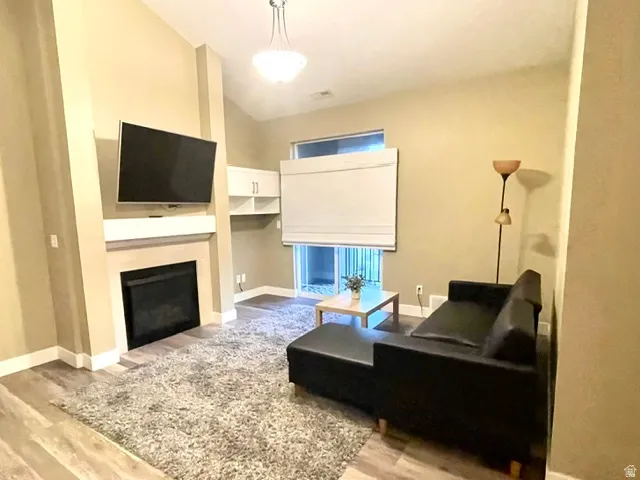 Vaulted ceiling, built-in fireplace with mantel, wood-finish flooring, built-in shelving, and a glass-paneled door