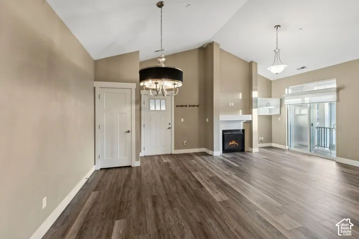 Unfurnished living room with dark wood-style floors, a high ceiling, hanging lights, and a warm lit fireplace