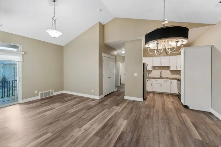 Kitchen with suspended lighting, white cabinetry, vaulted ceiling, dark wood-style floors, and backsplash
