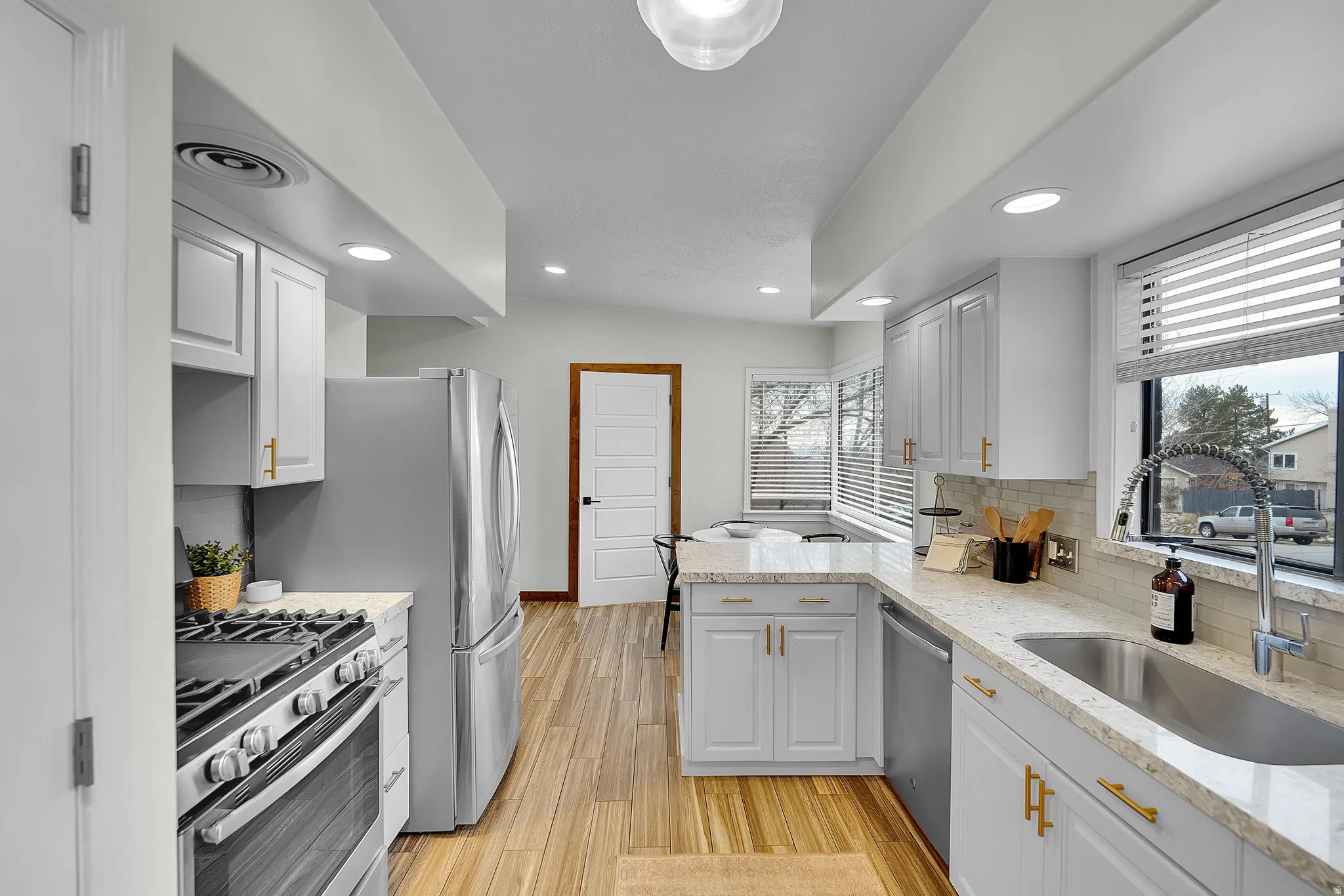 Kitchen with stainless steel appliances, a peninsula, light stone counters, decorative backsplash, and light wood-style floors