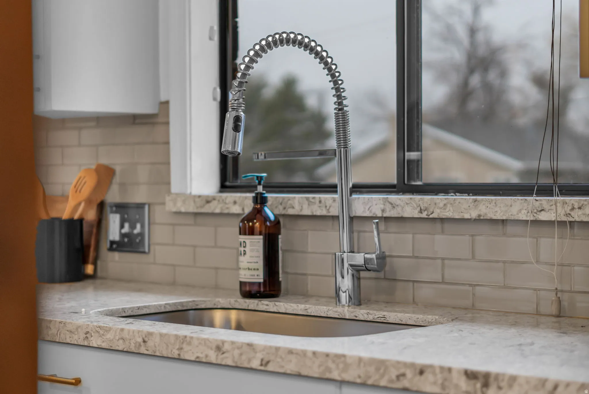 Kitchen view of backsplash, light stone counters, and white cabinetry