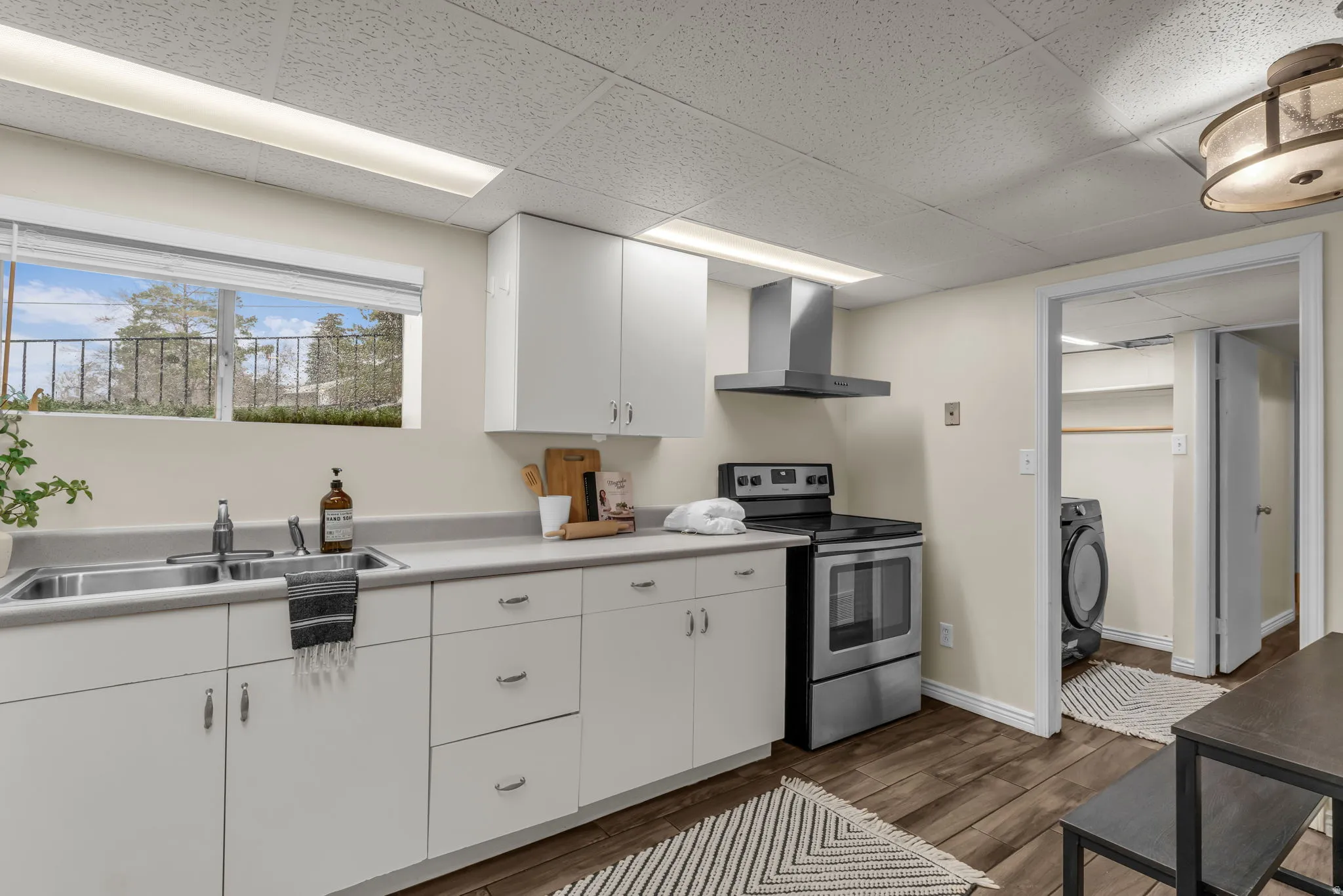 Kitchen with stainless steel electric stove, white cabinets, light countertops, dark wood-type flooring, and a paneled ceiling