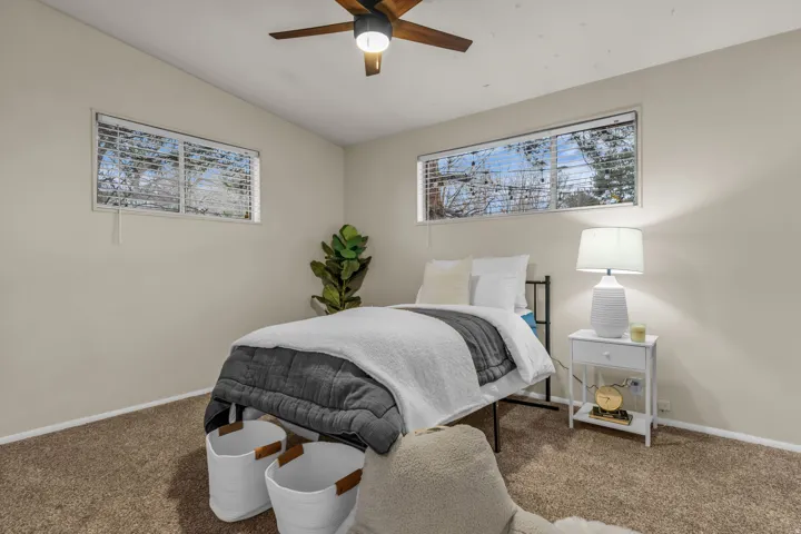 Bedroom with vaulted ceiling, carpet flooring, ceiling fan, and multiple windows