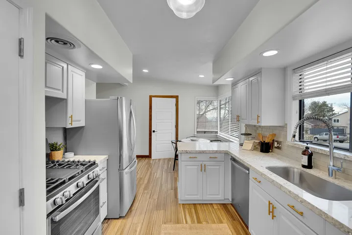 Kitchen with stainless steel appliances, a peninsula, light stone counters, decorative backsplash, and light wood-style floors
